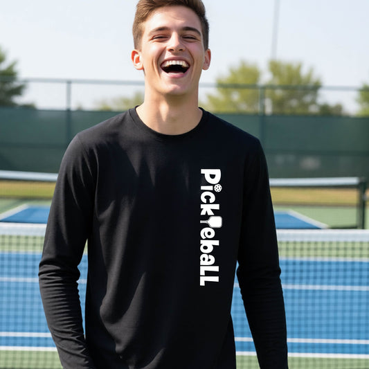 A young person wearing a black long-sleeve t-shirt with a white graphic text 'PICKLEBALL' with a pickleball paddle replacing the L, on the front, standing on a pickleball court.