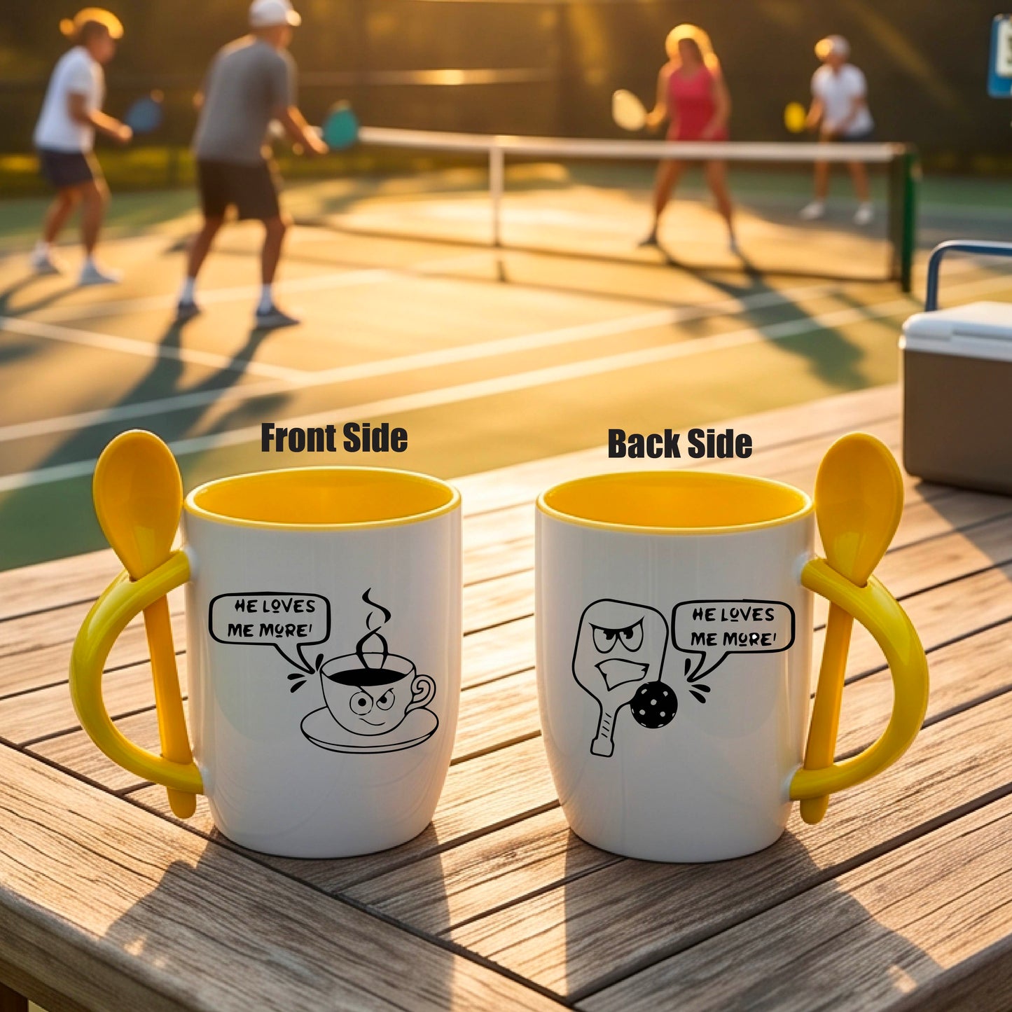 A white and yellow 12 ounce coffee mug with a built in spoon in the handle with and a fun pickleball paddle and ball and coffee cup graphic and the text “HE LOVES ME MORE”