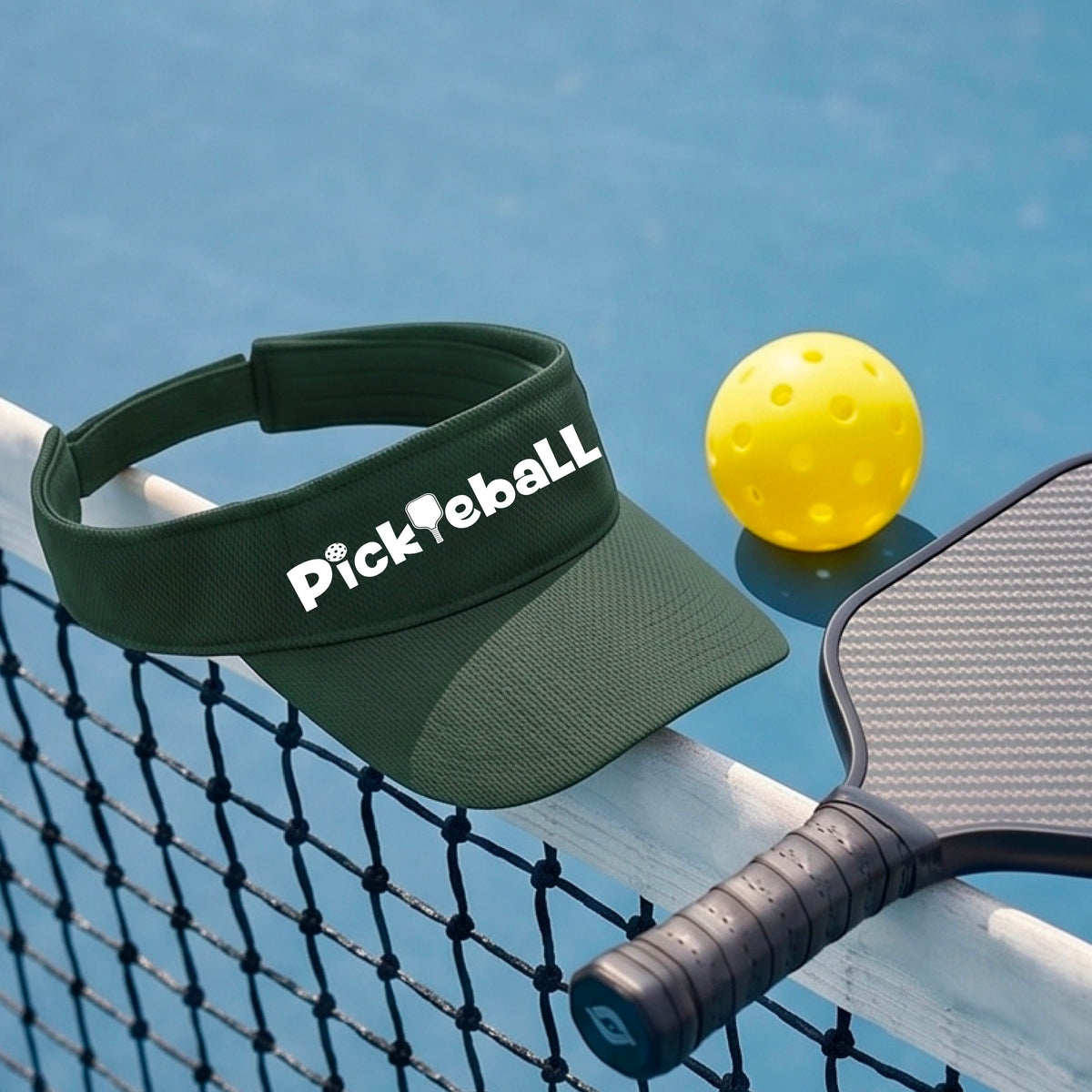 A close-up of a green athletic visor with a white graphic text 'PICKLEBALL' with a pickleball paddle replacing the L, on a pickleball court.