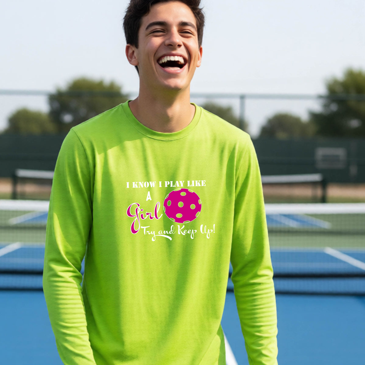 A young person laughing while wearing a lime green long-sleeve t-shirt with a pink and white graphic that reads 'I KNOW I PLAY LIKE A Girl Try and Keep Up!' with a pink pickleball illustration.