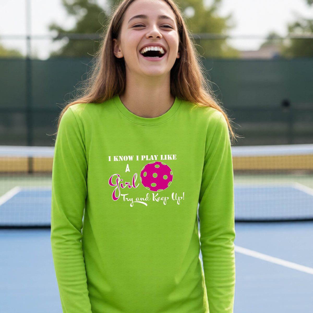 A young person laughing while wearing a lime green long-sleeve t-shirt with a pink and white graphic that reads 'I KNOW I PLAY LIKE A Girl Try and Keep Up!' with a pink pickleball illustration.