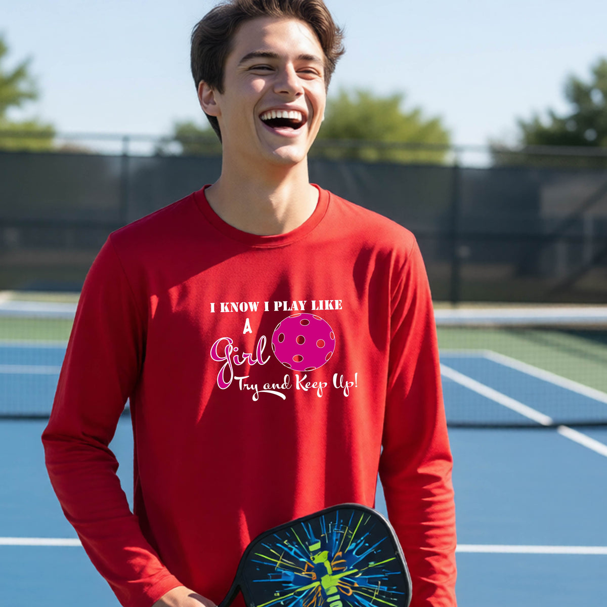A young person laughing while wearing a red long-sleeve t-shirt with a pink and white graphic that reads 'I KNOW I PLAY LIKE A Girl Try and Keep Up!' with a pink pickleball illustration.
