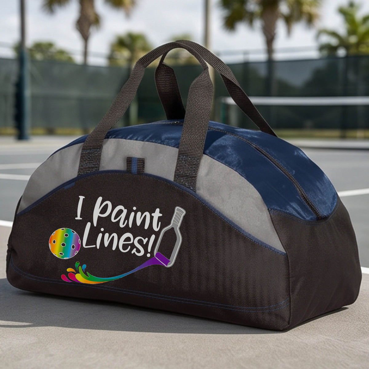 A close-up of navy blue, gray and black medium size duffel bag with a graphic on the front that has white text "I PAINT LINES'  with a white pickleball paddle painting multi-colored lines leading a mutli-colored pickleball.