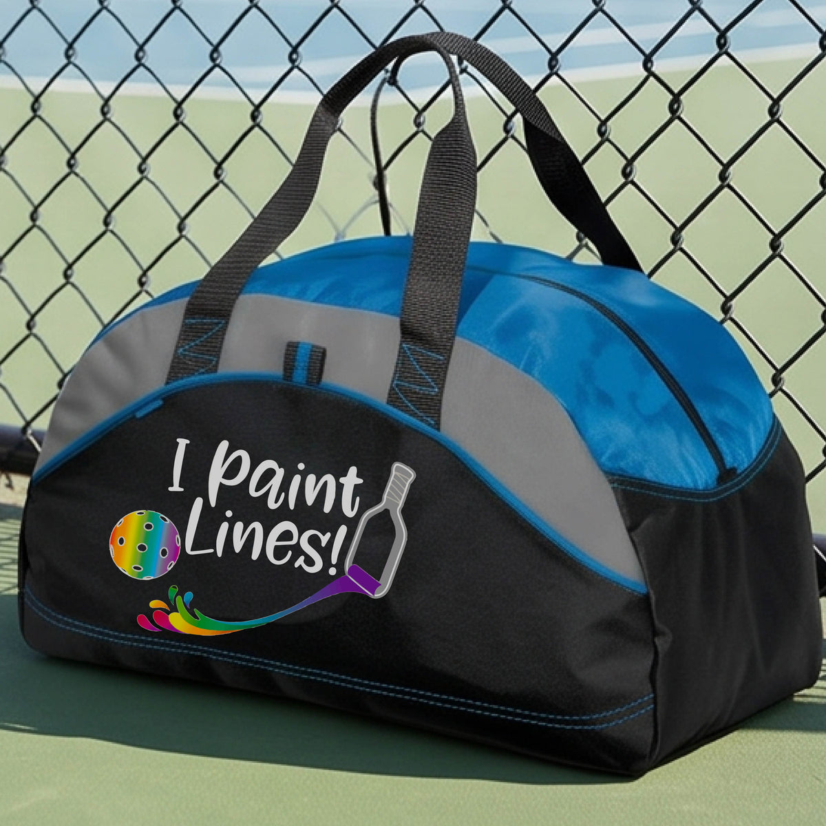 A close-up of blue, gray and black medium size duffel bag with a graphic on the front that has white text "I PAINT LINES'  with a white pickleball paddle painting multi-colored lines leading a mutli-colored pickleball.