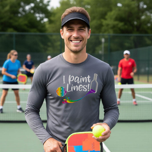A close-up of a man wearing a gray long-sleeve t-shirt with a graphic on the front that has white text "I PAINT LINES'  with a white pickleball paddle painting multi-colored lines leading a mutli-colored pickleball.