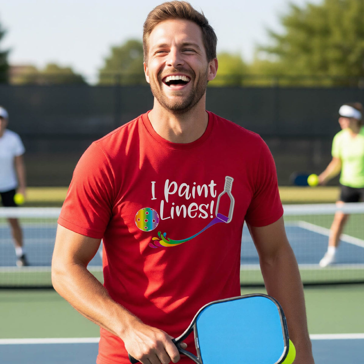 A close-up of a woman wearing a red short-sleeve t-shirt with a graphic on the front that has white text "I PAINT LINES'  with a white pickleball paddle painting multi-colored lines leading a mutli-colored pickleball.