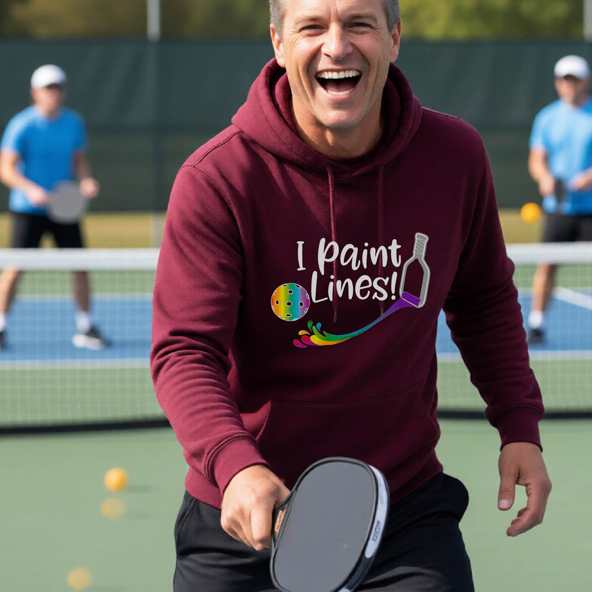 A man on an outdoor pickleball court wearing a maroon unisex hoodie pullover with a graphic that reads 'THIS IS MY PICKLEBALL SHIRT' in white with a yellow pickleball graphic on the back.