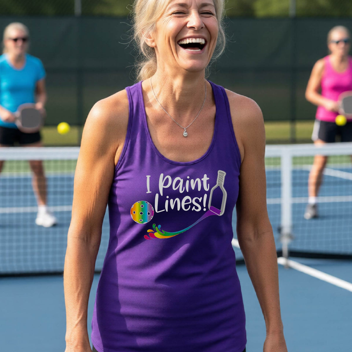A close-up of a woman wearing a purple racerback tank top with a graphic on the front that has white text "I PAINT LINES'  with a white pickleball paddle painting multi-colored lines leading a mutli-colored pickleball.