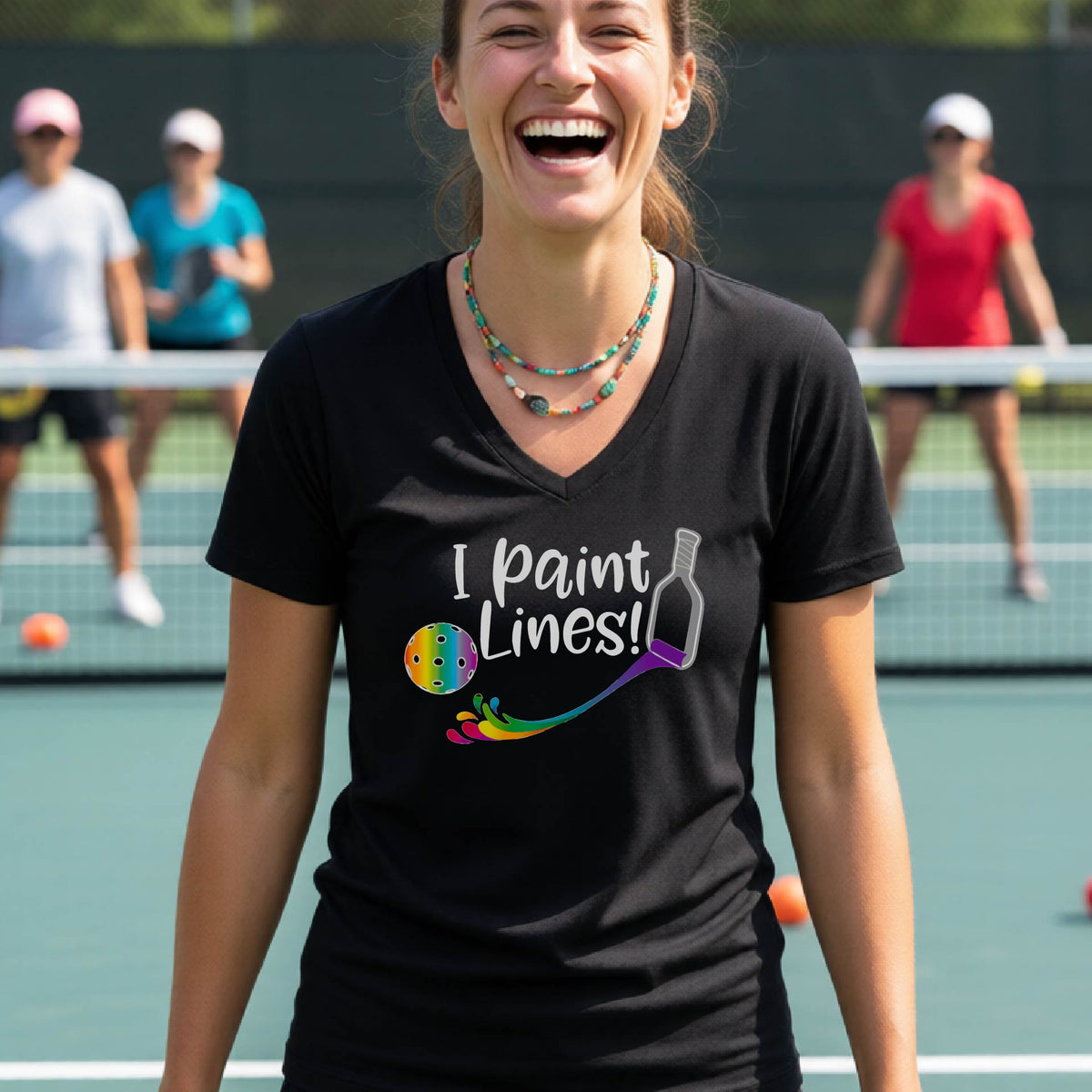 A woman on a pickleball court wearing a black V-neck t-shirt with the graphic 'I paint Lines!' and a paintbrush illustration. 