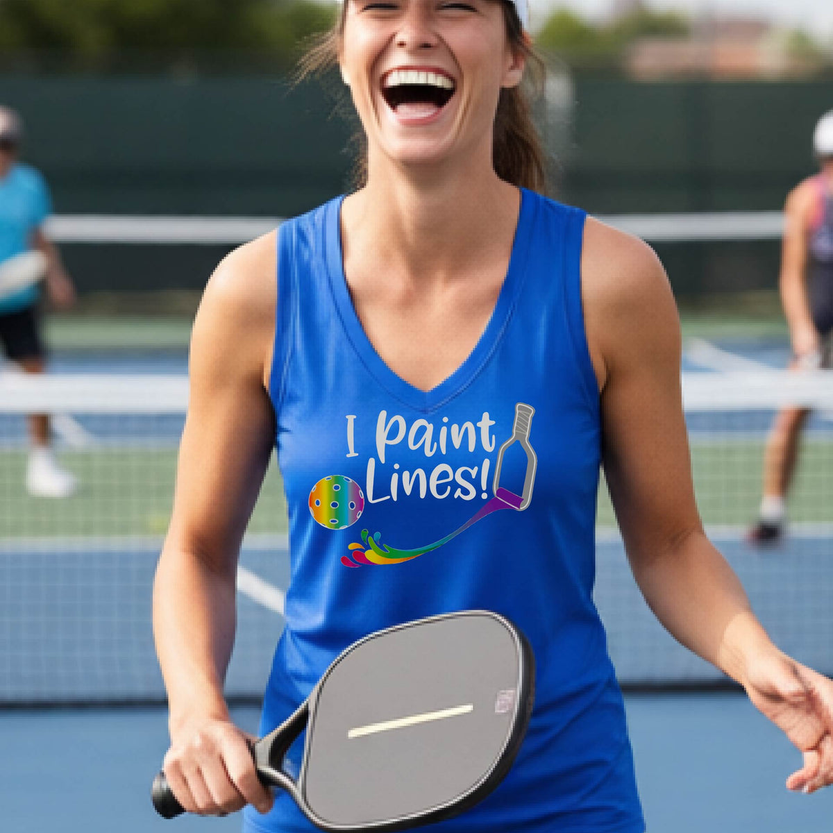 A close-up of a woman wearing a royal blue sleeveless t-shirt with a graphic on the front that has white text "I PAINT LINES'  with a white pickleball paddle painting multi-colored lines leading a mutli-colored pickleball.