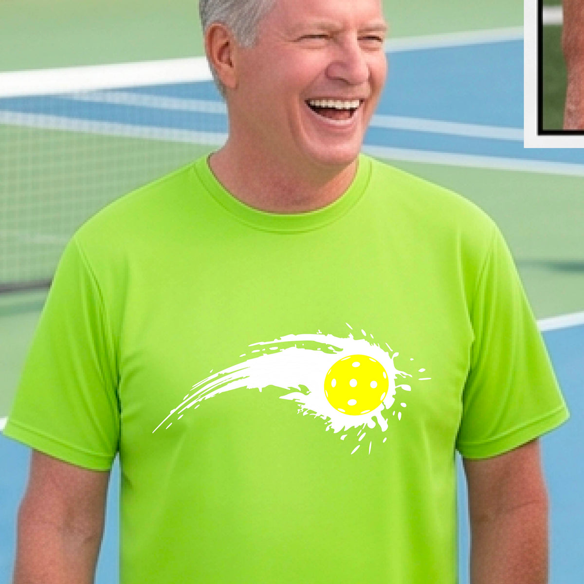 A man wearing a lime green short-sleeve T-shirt with a white pickleball graphic of a yellow pickleball with a motion trail effect, displayed in front of a pickleball court. 