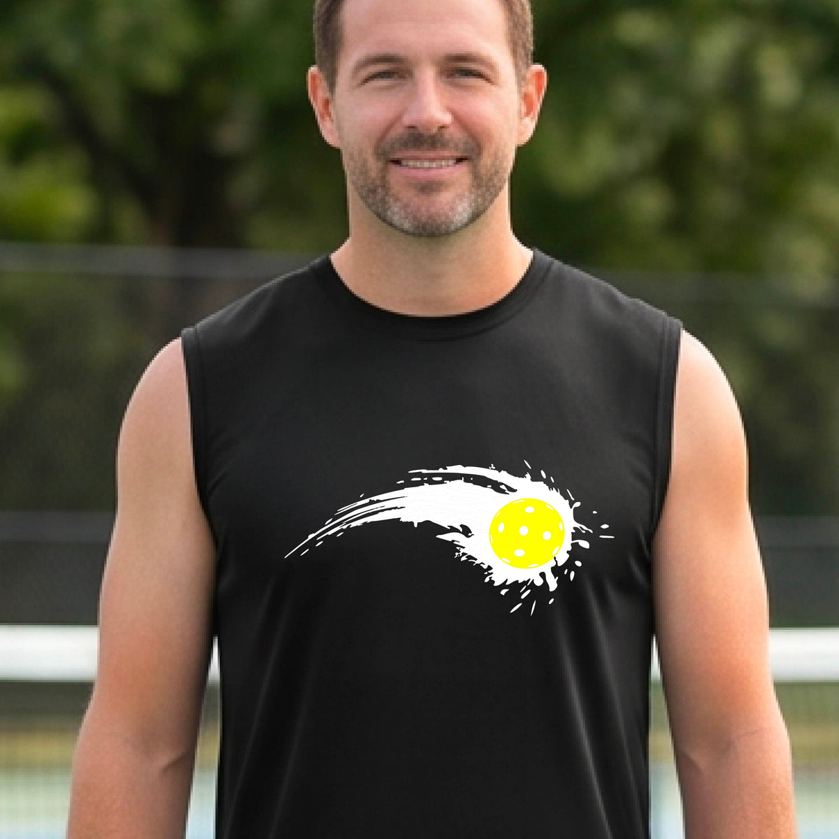 A man wearing a black sleeveless T-shirt with a white pickleball graphic of a yellow pickleball with a motion trail effect, displayed in front of a pickleball court. 