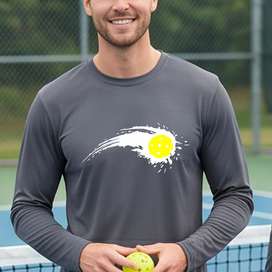 A man wearing a gray  long-sleeve T-shirt with a white pickleball graphic of a yellow pickleball with a motion trail effect, displayed in front of a pickleball court. 