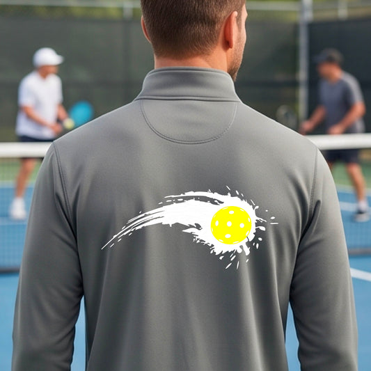 A man wearing a gray long-sleeve quarter-zip shirt with a white pickleball graphic of a yellow pickleball with a motion trail effect, displayed in front of a pickleball court. 