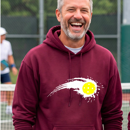 A man wearing a maroon unisex hoodie pullover with a white pickleball graphic of a yellow pickleball with a motion trail effect, displayed in front of a pickleball court. 