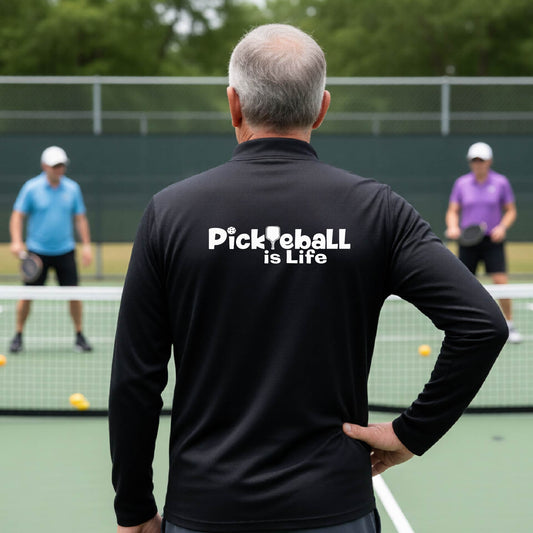 A man viewed from behind on a pickleball court, wearing a black long-sleeve shirt with the white text 'Pickleball is Life' printed across the back.