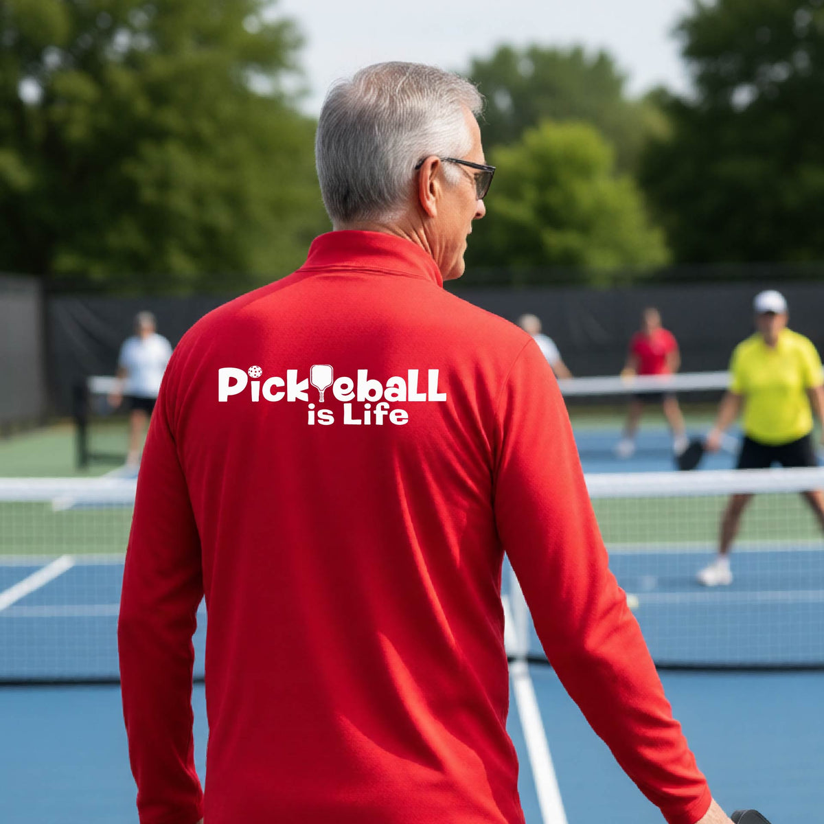 A man viewed from behind on a pickleball court, wearing a red long-sleeve shirt with the white text 'Pickleball is Life' printed across the back.