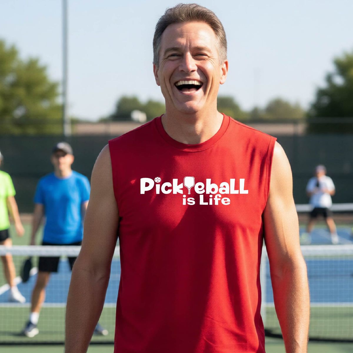 A smiling man on a pickleball court wearing a red sleeveless shirt with the text 'PickYeball is Life' in white.