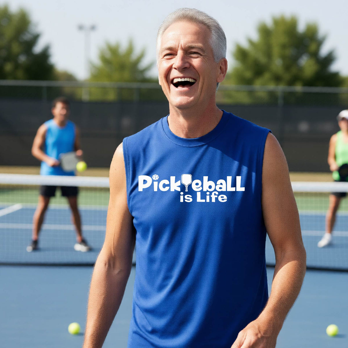 A smiling man on a pickleball court wearing a royal blue sleeveless shirt with the text 'PickYeball is Life' in white.