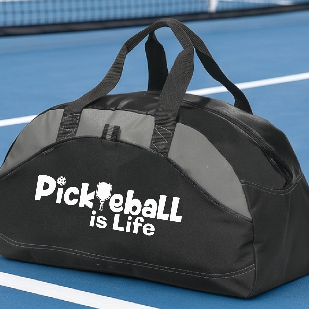 A black, and gray duffel bag with the text 'Pickbeall is Life' printed on the front, placed on a tennis court.