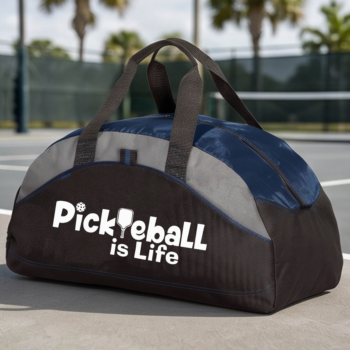 A navy blue, black, and gray duffel bag with the text 'Pickbeall is Life' printed on the front, placed on a tennis court.