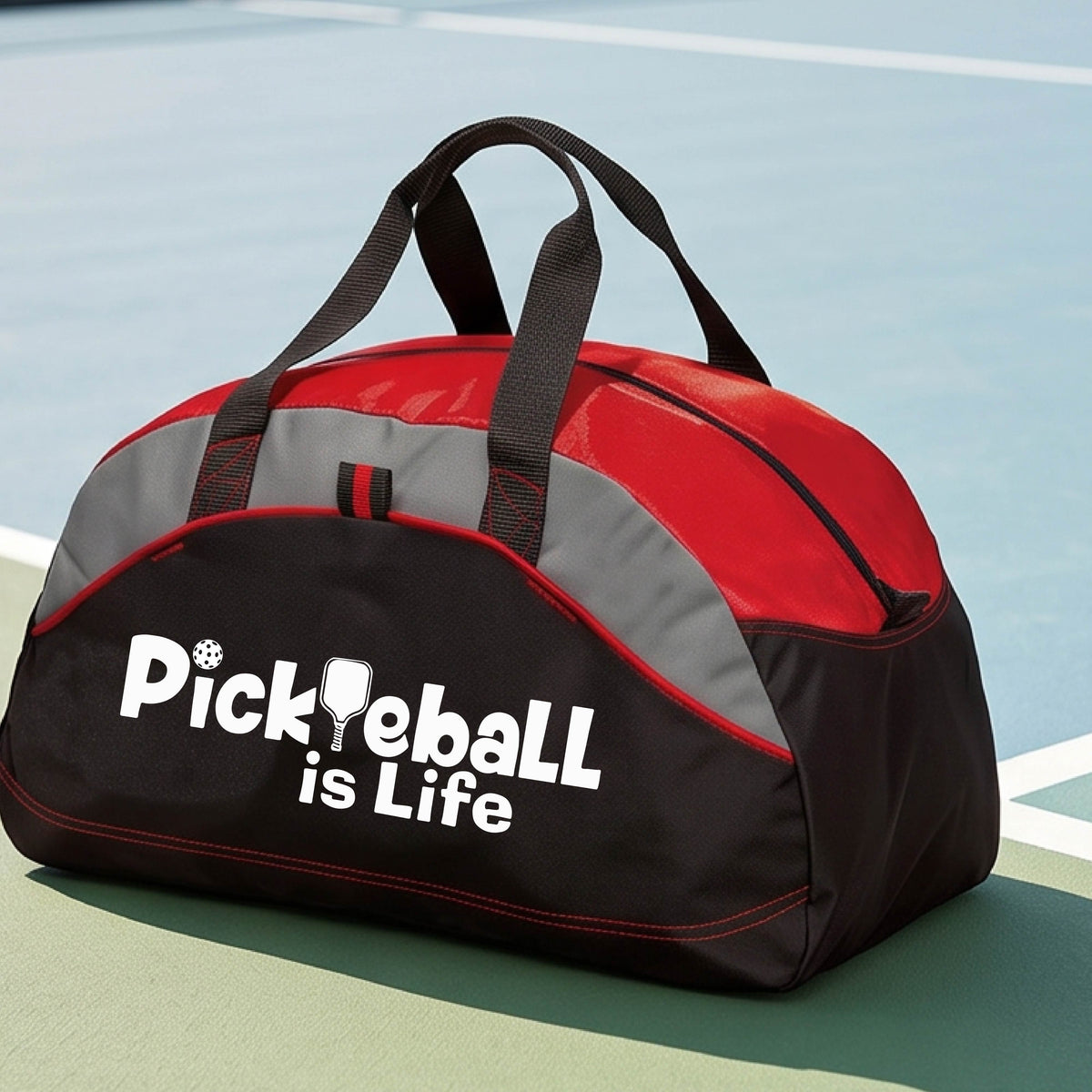 A red, black, and gray duffel bag with the text 'Pickbeall is Life' printed on the front, placed on a tennis court.