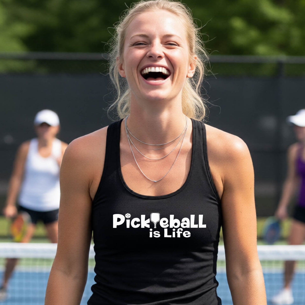 A woman wearing a black racerback tank top with the slogan 'Pickleball is Life' printed in white across the back, with a pickleball paddle replacing the L. 
