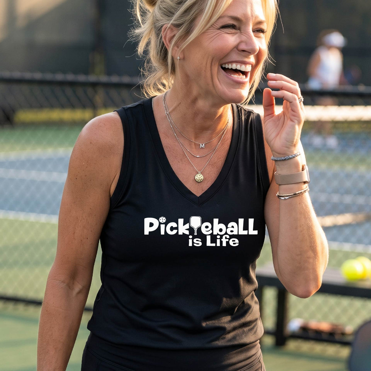A woman wearing a black sleeveless v-neck t-shirt with the slogan 'Pickleball is Life' printed in white across the back, with a pickleball paddle replacing the L.