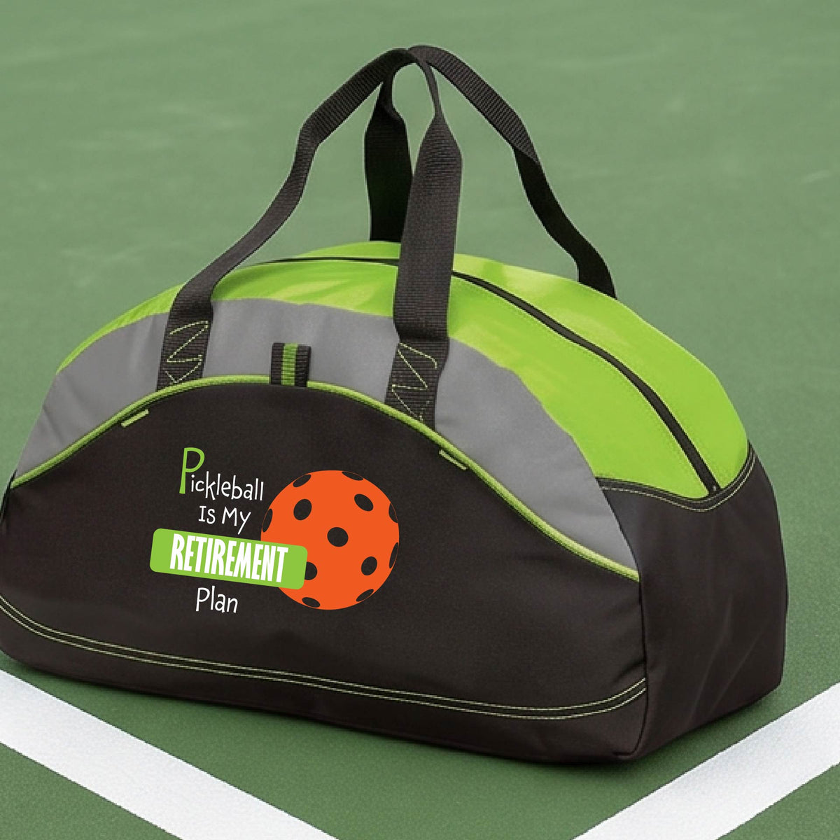 A close-up of a lime green and black duffel bag with gray panels. on a pickleball court, with a graphic of the words “Pickleball is my Retirement Plan” in green and white with an orange pickleball illustration in the background.
