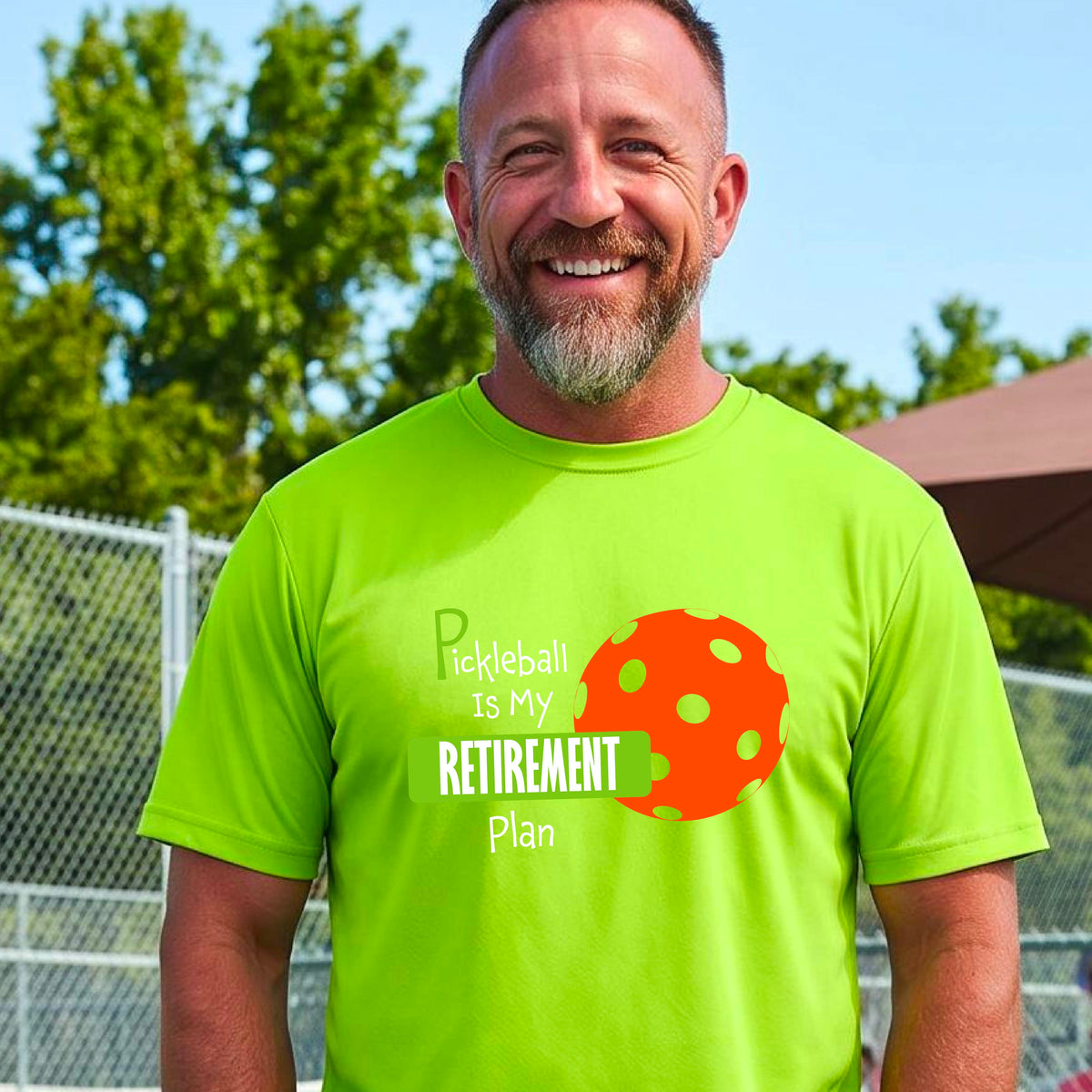 A man on a pickleball court, wearing a lime green short-sleeve athletic t-shirt, with the words “Pickleball is my Retirement Plan” in green and white with an orange pickleball illustration in the background