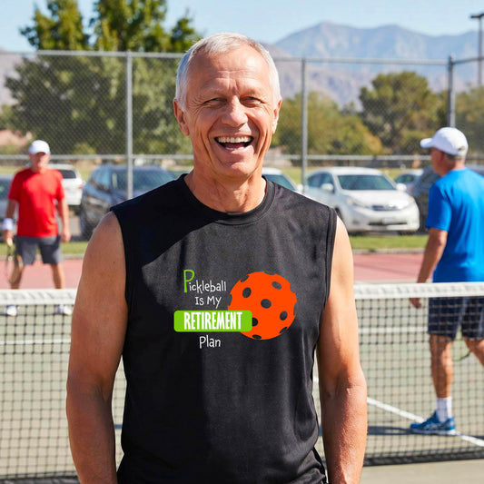 A man on a pickleball court, wearing a black sleeveless athletic t-shirt, with the words “Pickleball is my Retirement Plan” in green and white with an orange pickleball illustration in the background.
