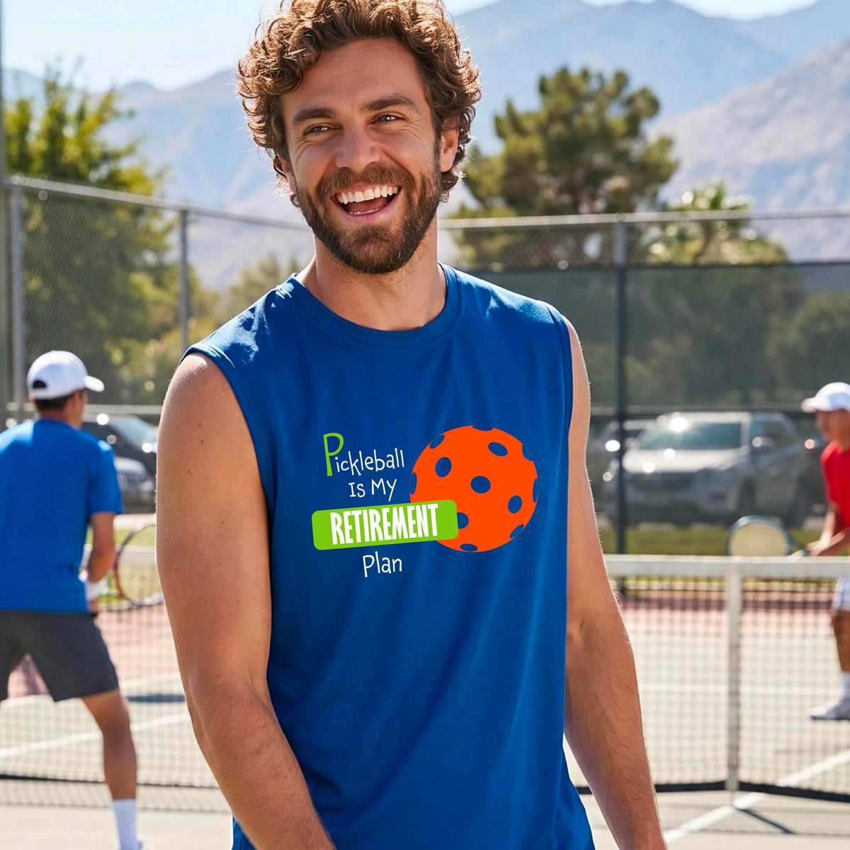 A man on a pickleball court, wearing a royal blue sleeveless athletic t-shirt, with the words “Pickleball is my Retirement Plan” in green and white with an orange pickleball illustration in the background.