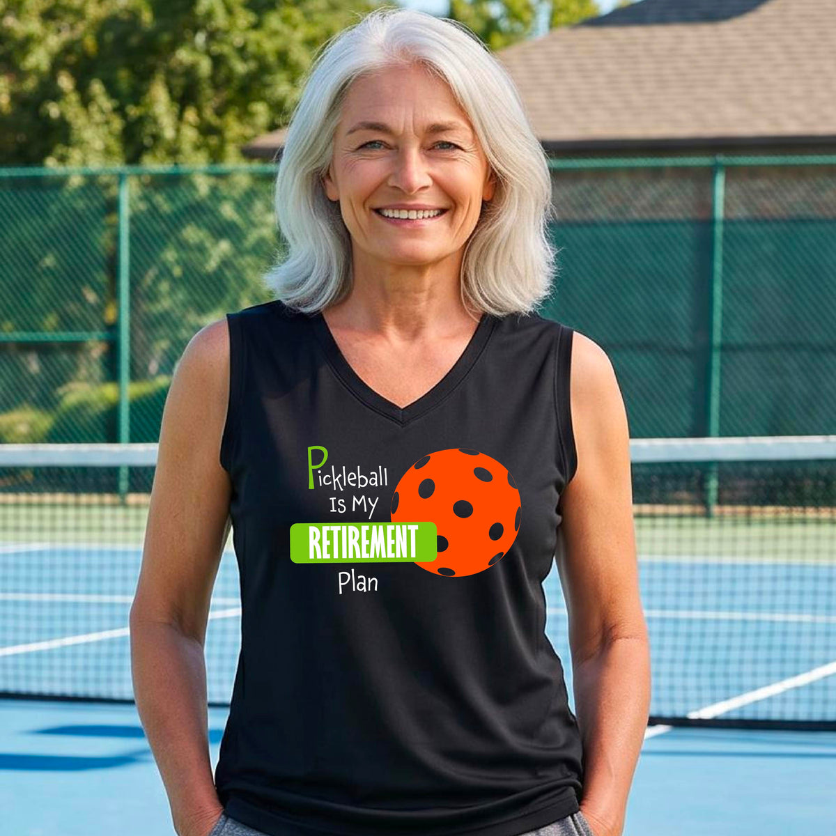 A woman on a pickleball court, wearing a black sleeveless v-neck athletic t-shirt, with the words “Pickleball is my Retirement Plan” in green and white with an orange pickleball illustration in the background