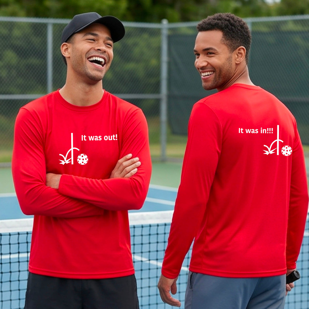 Two men showing a red long-sleeve t-shirt with a white design of ‘IT WAS OUT!’ and a colorful pickleball on the front, and the back design with a white ‘IT WAS IN!!!’ and a colorful pickleball, standing on a pickleball court.