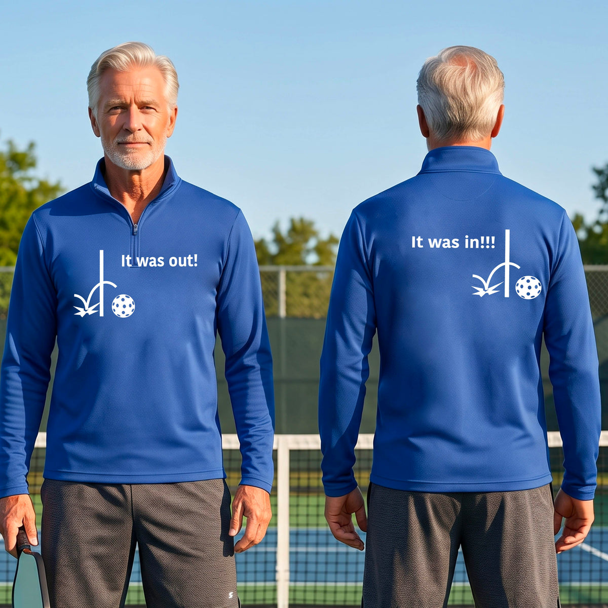 Two men wearing a royal blue quarter-zip shirt with a white design of ‘IT WAS OUT!’ and a colorful pickleball on the front, and the back design with a white ‘IT WAS IN!!!’ and a colorful pickleball, standing on a pickleball court.