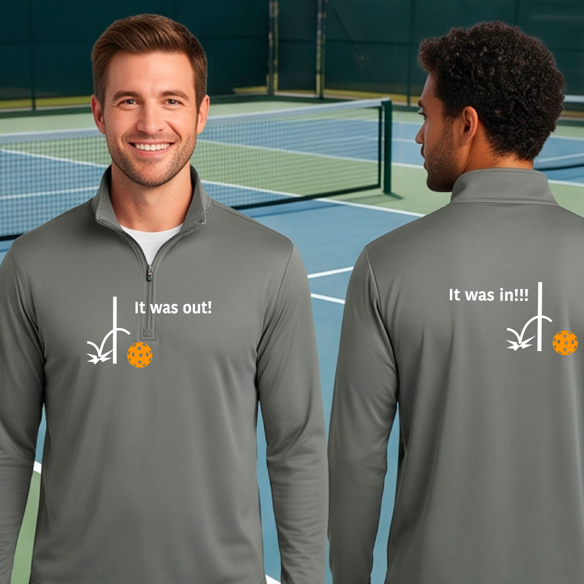 Two men wearing a gray quarter-zip shirt with a white design of ‘IT WAS OUT!’ and a colorful pickleball on the front, and the back design with a white ‘IT WAS IN!!!’ and a colorful pickleball, standing on a pickleball court.