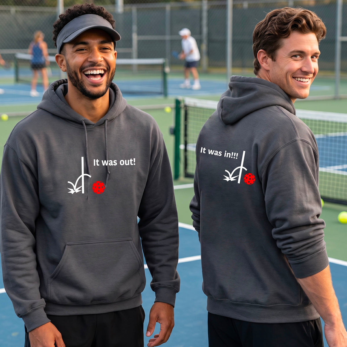 Two men showing a gray hoodie pullover with a white design of ‘IT WAS OUT!’ and a colorful pickleball on the front, and the back design with a white ‘IT WAS IN!!!’ and a colorful pickleball, standing on a pickleball court.
