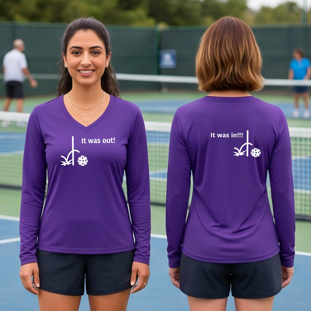 Two women wearing a purple long-sleeve t-shirt with a white design of ‘IT WAS OUT!’ and a colorful pickleball on the front, and the back design with a white ‘IT WAS IN!!!’ and a colorful pickleball, standing on a pickleball court.