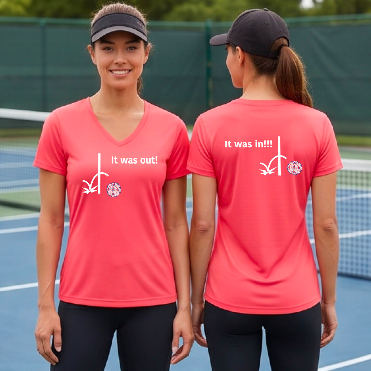Two women showing a coral pink short-sleeve t-shirt with a white design of ‘IT WAS OUT!’ and a colorful pickleball on the front, and the back design with a white ‘IT WAS IN!!!’ and a colorful pickleball, standing on a pickleball court.