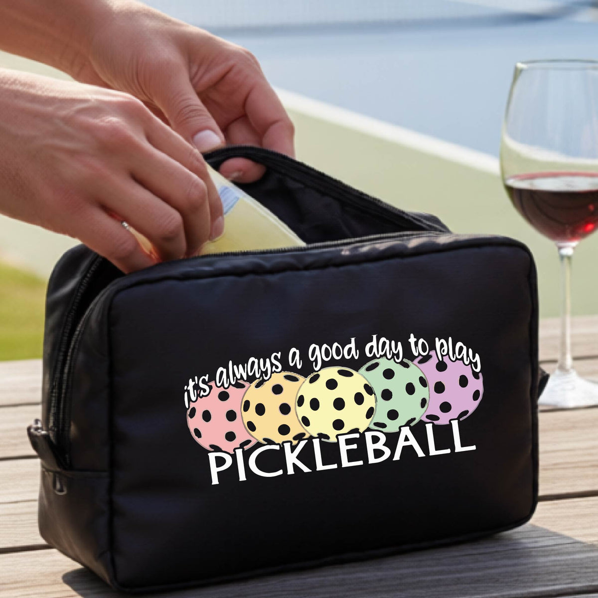 A black pickleball-themed zippered cosmetic pouch with a printed graphic and the phrase 'it's always a good day to play PICKLEBALL' .