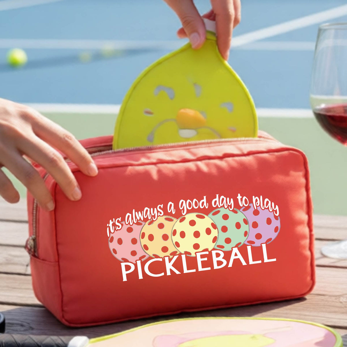 A coral pickleball-themed zippered cosmetic pouch with a printed graphic and the phrase 'it's always a good day to play PICKLEBALL' .