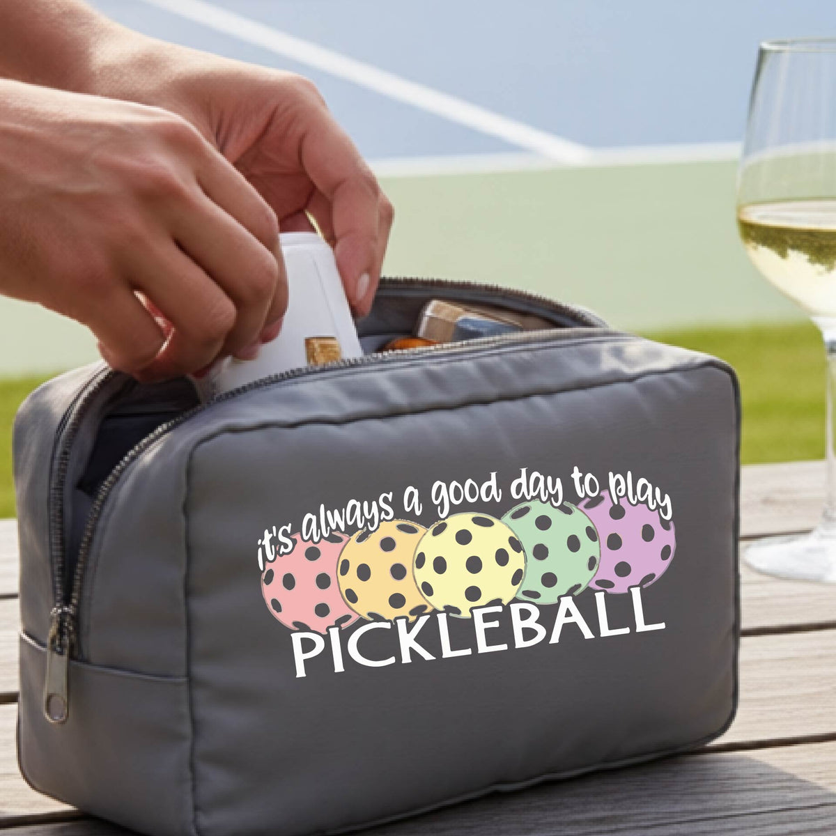 A gray pickleball-themed zippered cosmetic pouch with a printed graphic and the phrase 'it's always a good day to play PICKLEBALL' .