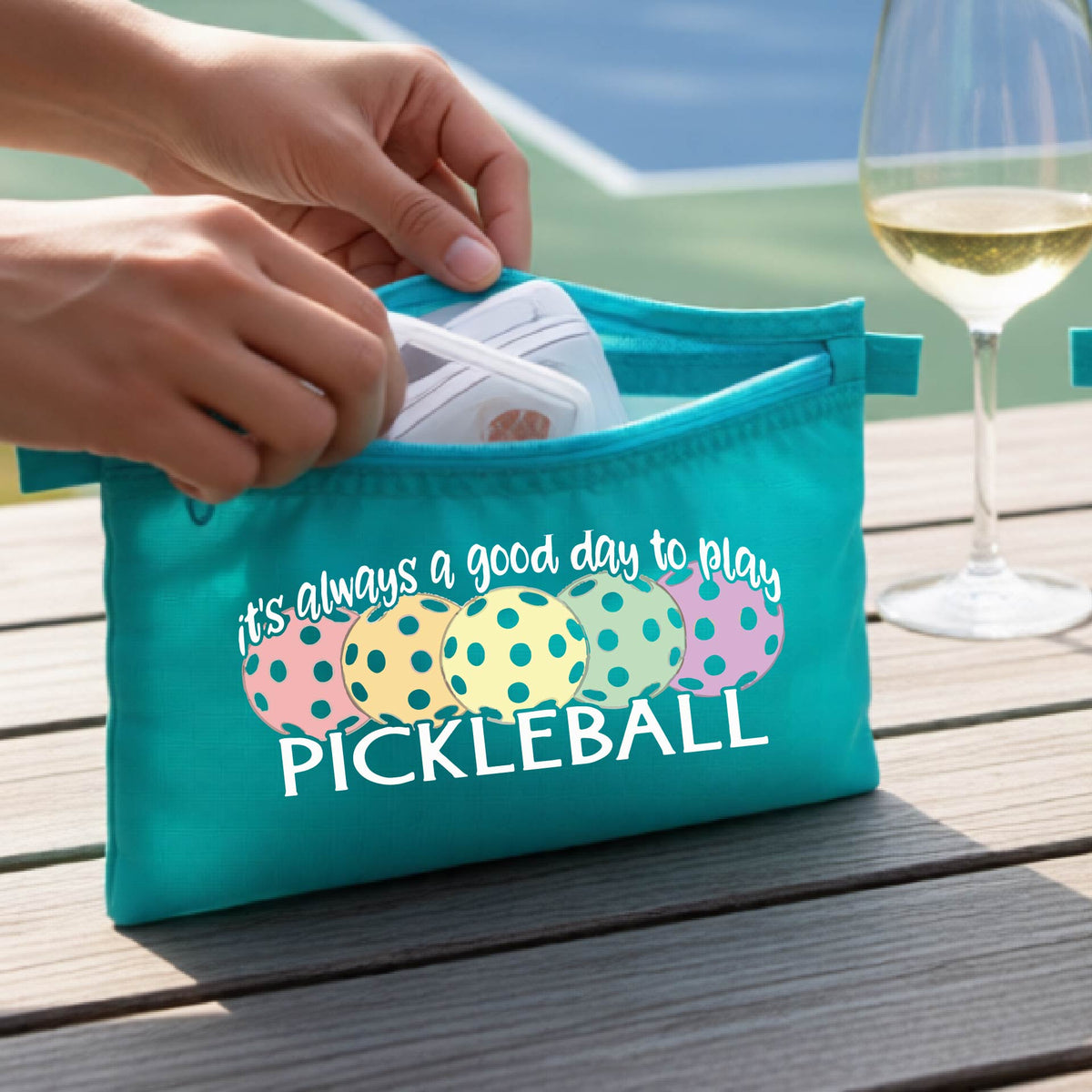 A turquoise polyester pickleball bag and a graphic of colorful  pickleballs and the text 'it's always a good day to play PICKLEBALL'.