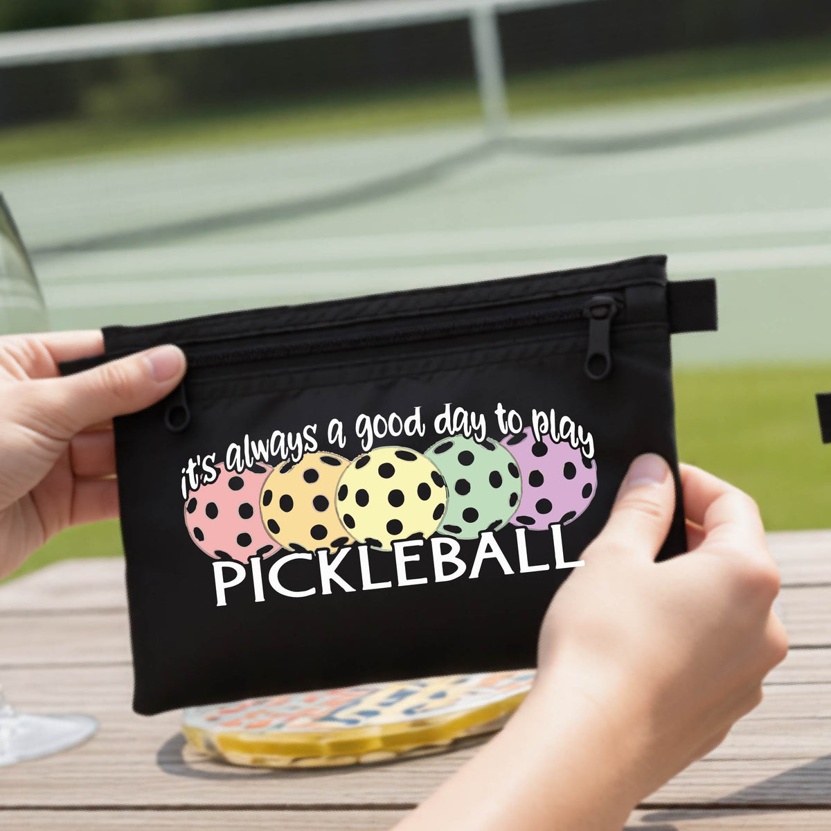 A black polyester pickleball bag and a graphic of colorful  pickleballs and the text 'it's always a good day to play PICKLEBALL'.