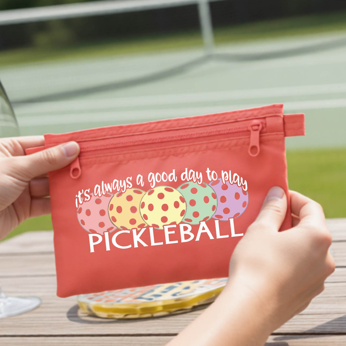 A coral-colored polyester pickleball bag and a graphic of colorful  pickleballs and the text 'it's always a good day to play PICKLEBALL'.