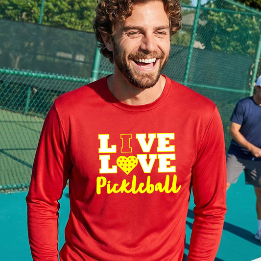 A man on a pickleball court wearing a red long-sleeve V-neck shirt with a yellow graphic that reads 'LIVE LOVE Pickleball' and a heart-shaped pickleball dot pattern inside the word 'LOVE'.