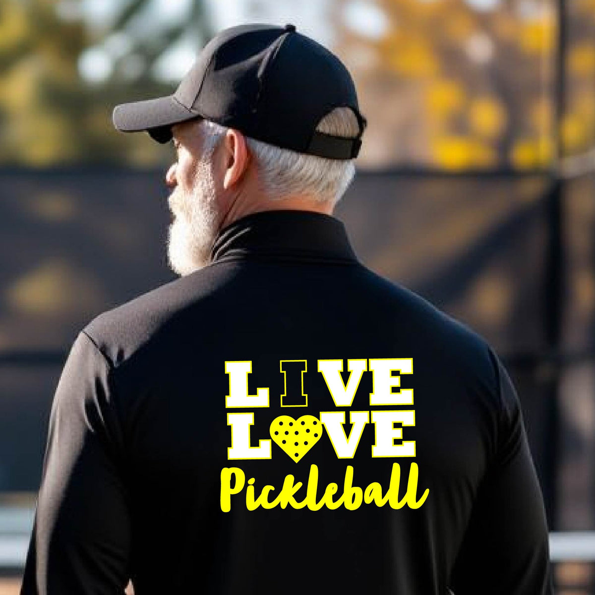 A man viewed from behind wearing a black long-sleeve athletic quarter-zip shirt with a yellow graphic on the back that reads 'LIVE LOVE Pickleball'  with a pickleball motiff heart for replacing the O,set against an outdoor blurred background.