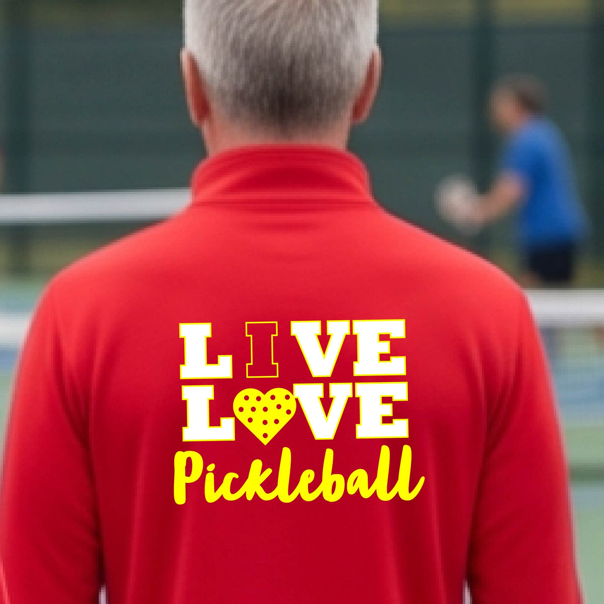 A man viewed from behind wearing a red long-sleeve athletic quarter-zip shirt with a yellow graphic on the back that reads 'LIVE LOVE Pickleball'  with a pickleball motiff heart for replacing the O,set against an outdoor blurred background.