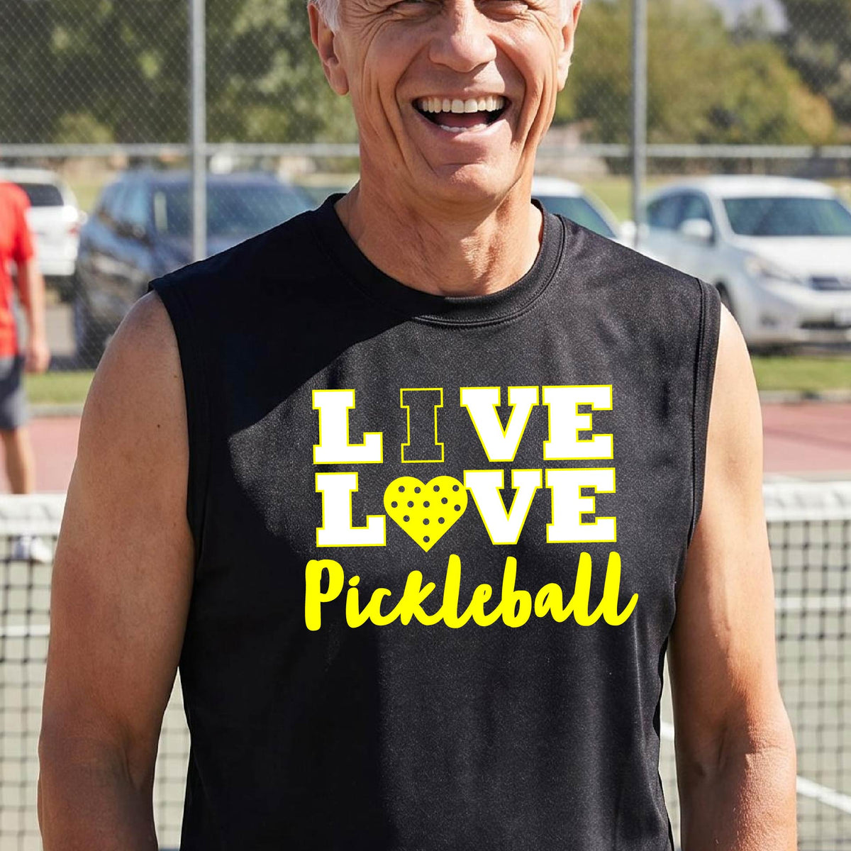 A man on a pickleball court wearing a lime black sleeveless V-neck shirt with a yellow graphic that reads 'LIVE LOVE Pickleball' and a heart-shaped pickleball dot pattern inside the word 'LOVE'.