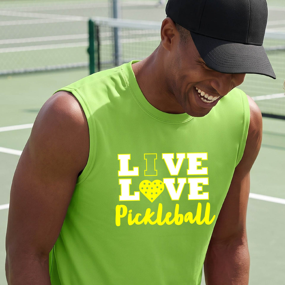 A man on a pickleball court wearing a lime green sleeveless V-neck shirt with a yellow graphic that reads 'LIVE LOVE Pickleball' and a heart-shaped pickleball dot pattern inside the word 'LOVE'.